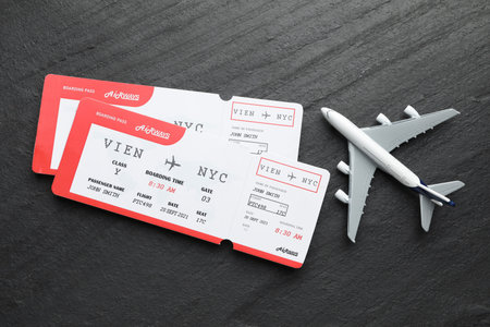 Travel agency. Flight tickets and plane model on dark textured table, flat lay