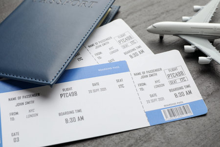 Travel agency. Flight tickets, passport and plane model on dark textured table, closeup