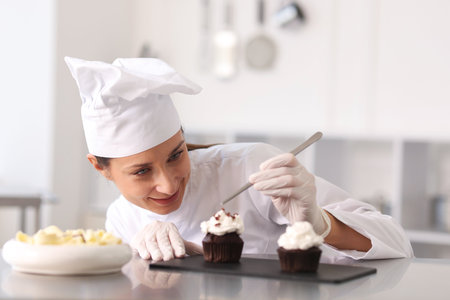 Confectioner decorating cupcake with pieces of chocolate in kitchenの写真素材
