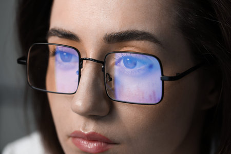 Young woman wearing glasses with reflection on dark background, closeup