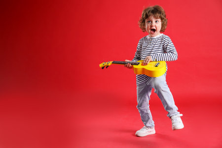 Cute little boy playing toy guitar on red background. Space for textの写真素材