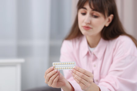 Upset woman with blister of contraceptive pills indoors, selective focus. Space for textの写真素材