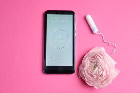 Smartphone with period calendar application, tampon and flower on pink background, flat layの写真素材