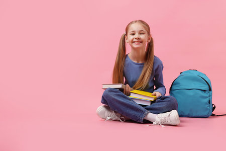 Schoolgirl with backpack and books on pink background. Space for textの写真素材