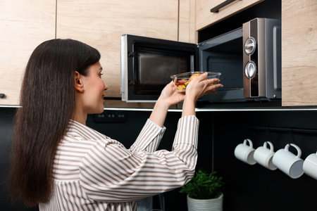 Woman putting container with lunch into microwave indoorsの写真素材