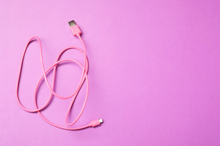 Pink USB charge cable on purple background, top view. Space for text