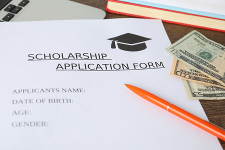 Scholarship application form, pen, laptop, books and dollar banknotes on wooden table, closeupの写真素材