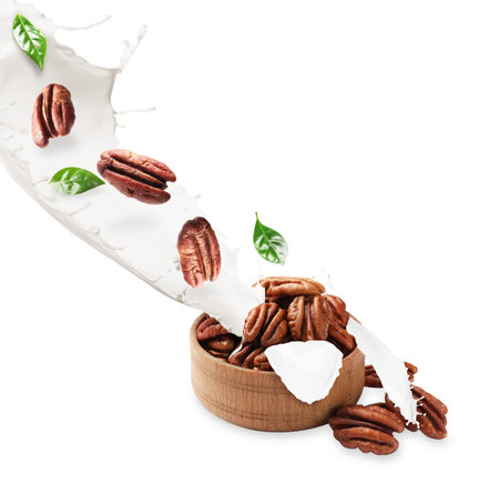 Nut milk with pecans and green leaves flowing into bowl on white background