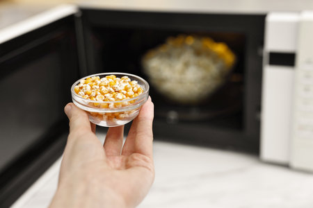 Woman with bowl of unpopped corn kernels near microwave oven indoors, closeup. Space for textの写真素材