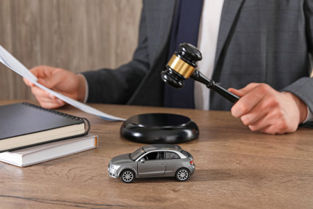 Auto accident law. Man with document and gavel at wooden table indoors, focus on toy carの写真素材