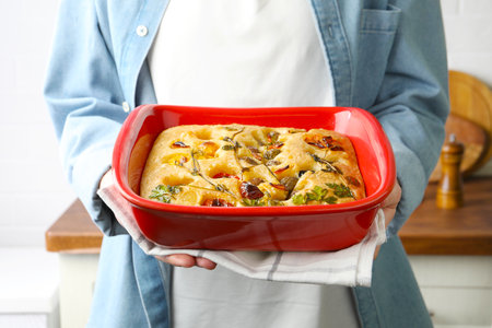 Woman holding focaccia with vegetables and olives in kitchen, closeupの写真素材