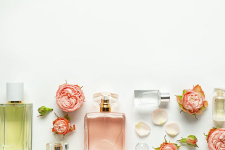 Bottles of aromatic perfume and beautiful flowers on white background, flat lay. Space for text
