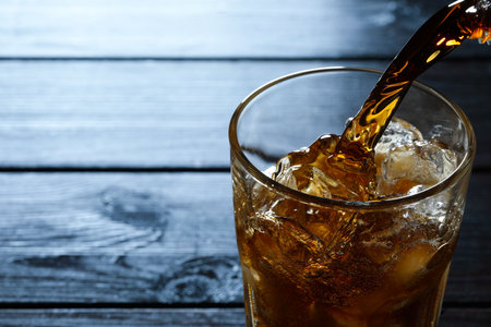 Pouring refreshing cola into glass at wooden table, closeup. Space for textの写真素材