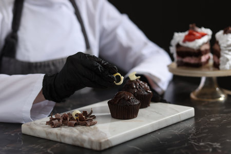 Confectioner decorating tasty chocolate muffins at black marble table in kitchen, closeupの写真素材
