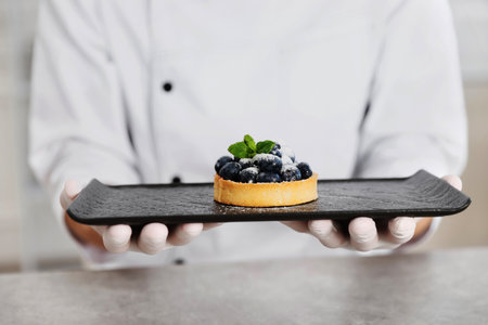 Confectioner with tasty tart at grey table in kitchen, closeupの写真素材