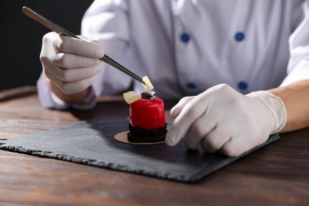 Confectioner decorating tasty dessert with chocolate shaving at wooden table, closeupの写真素材