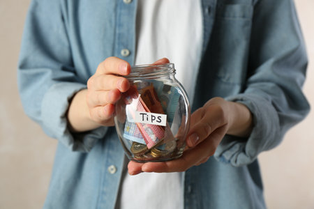 Woman holding tips jar with money on light background, closeupの写真素材