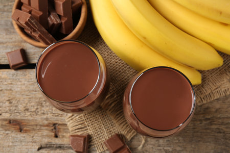 Tasty chocolate milk in glasses, pieces and bananas on wooden table, flat layの写真素材