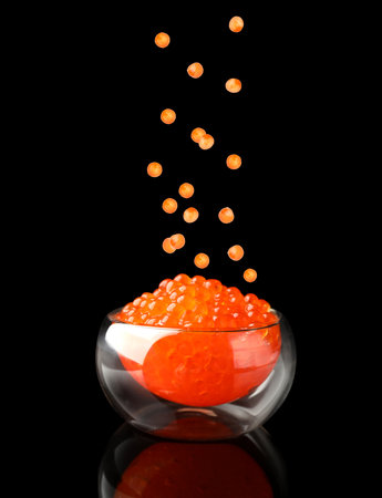 Red caviar falling into bowl on black background. Salmon roeの写真素材