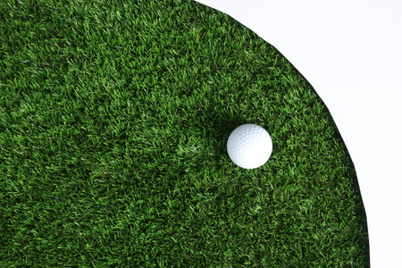 Golf ball and green grass on white background, top view