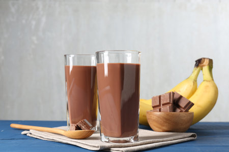 Tasty chocolate milk in glasses, pieces and bananas on blue wooden tableの写真素材