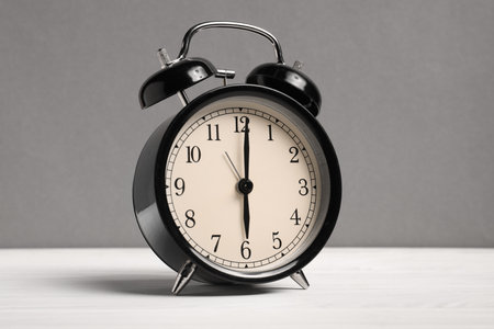 One black alarm clock on white wooden table against grey backgroundの写真素材