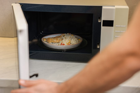 Man putting plate with lunch into microwave in kitchen, closeupの写真素材