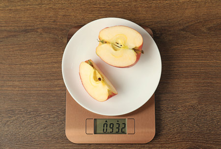 Modern electronic kitchen scale with cut apple on wooden table, top viewの写真素材