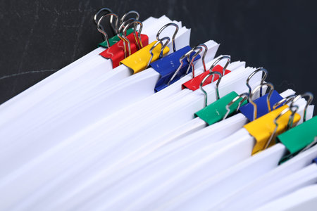 Binder clips with sheets of paper on black table, closeup
