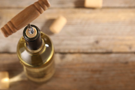 Bottle of luxury wine with corkscrew on table, closeup. Space for text