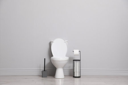 Ceramic toilet bowl, brush and paper near gray wall indoors. Space for textの写真素材