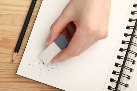 Woman rubbing eraser against paper at wooden table, top view