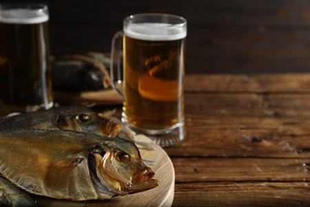 Dried fish and glasses of beer on wooden table, closeup. Space for text
