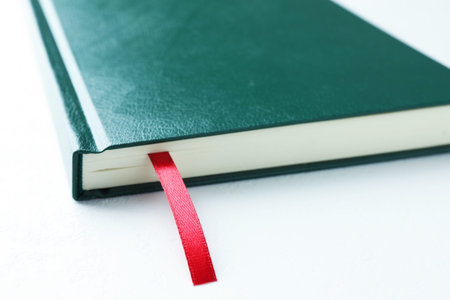 Book with red ribbon bookmark on white table, closeup