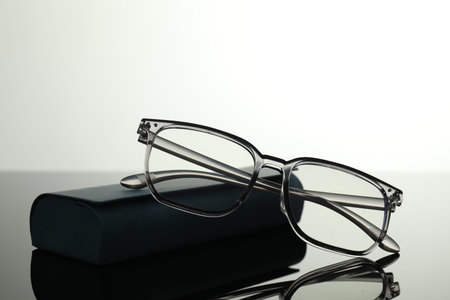 Stylish glasses and case on grey mirror surface, closeup. Space for text