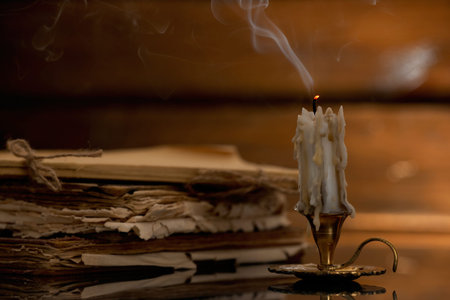 Smoldering candle in candlestick and old books on mirror surface, closeupの写真素材