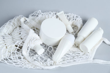 Many cosmetic products and mesh bag on light grey background