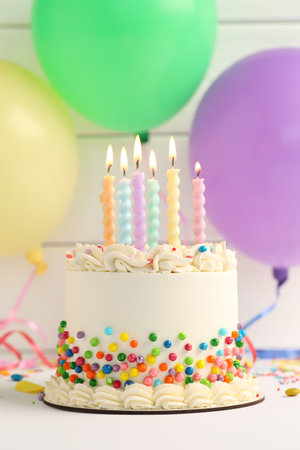 Delicious bento cake with colorful sprinkles and burning candles on white tableの写真素材