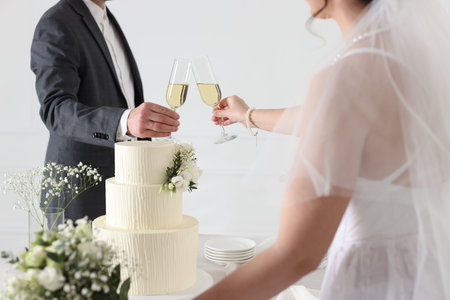 Married couple clinking glasses of champagne at table with wedding cake indoors, closeupの写真素材