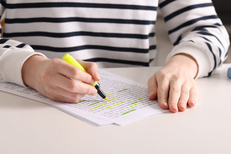 Woman highlighting important information at white desk indoors, closeup