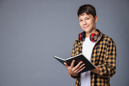 Portrait of teenage boy with book and headphones on grey background, space for textの写真素材