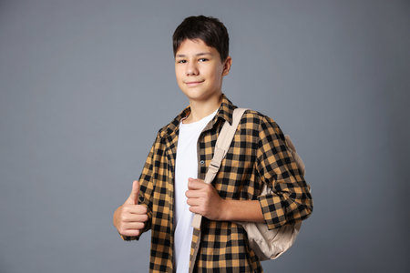 Portrait of teenage boy with backpack showing thumbs up on grey backgroundの写真素材