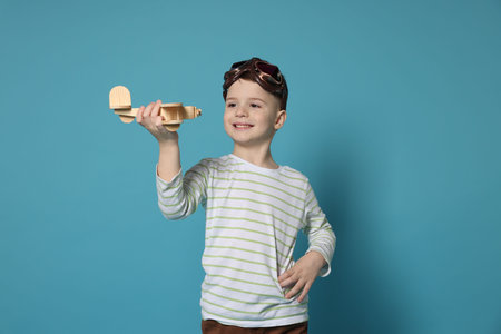 Happy little boy playing with toy plane on light blue backgroundの写真素材
