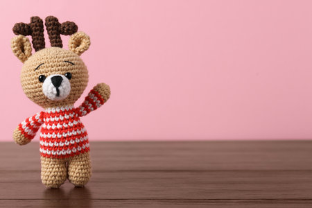 Cute knitted toy deer on wooden table against pink background. Space for textの写真素材