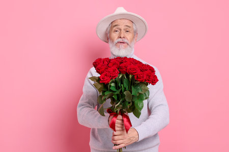 Senior man with bouquet of red roses on pink backgroundの写真素材