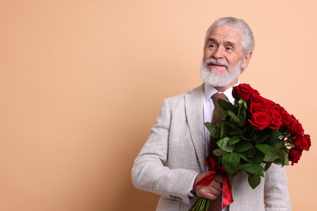 Senior man with bouquet of red roses on beige background, space for textの写真素材