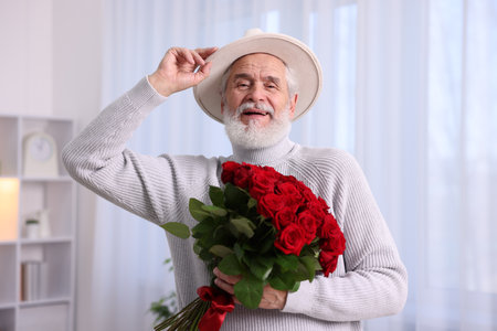 Senior man with bouquet of red roses at homeの写真素材