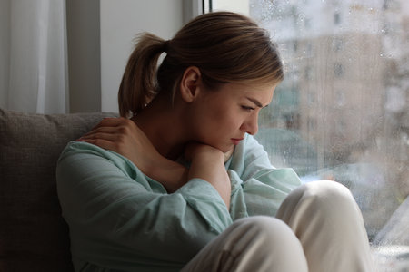 Depressed woman sitting near window at homeの写真素材