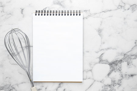 Blank recipe book and whisk on white marble table, top view. Mockup for designの写真素材