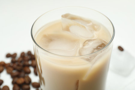 Coffee cream liqueur in glass and beans on white table, closeup